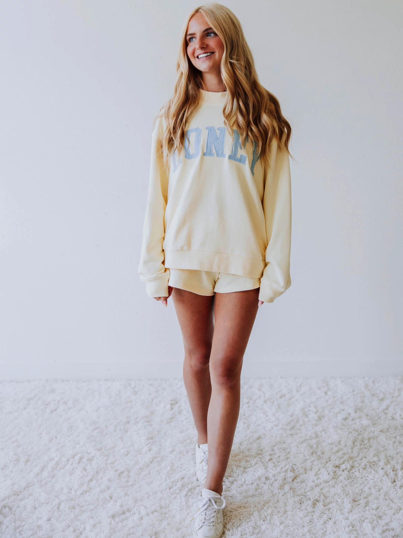 Girl wearing a soft, yellow two piece set. Top says HONEY on the front. The HONEY has blue lines going through each letter. Shorts are same yellow as top. 