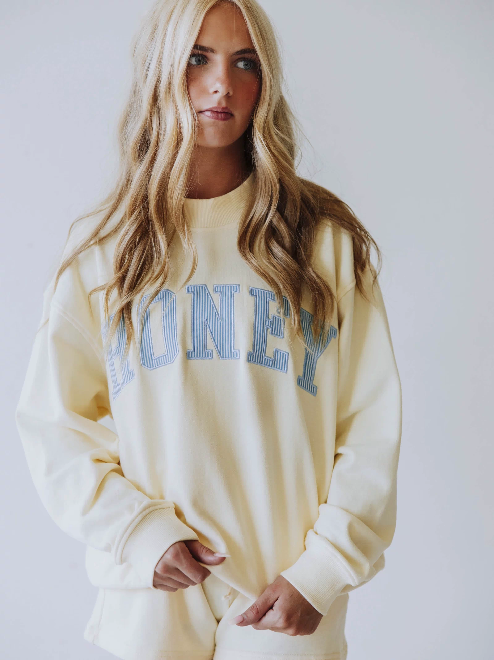 Girl wearing a soft, yellow two piece set. Top says HONEY on the front. The HONEY has blue lines going through each letter. Shorts are same yellow as top. 