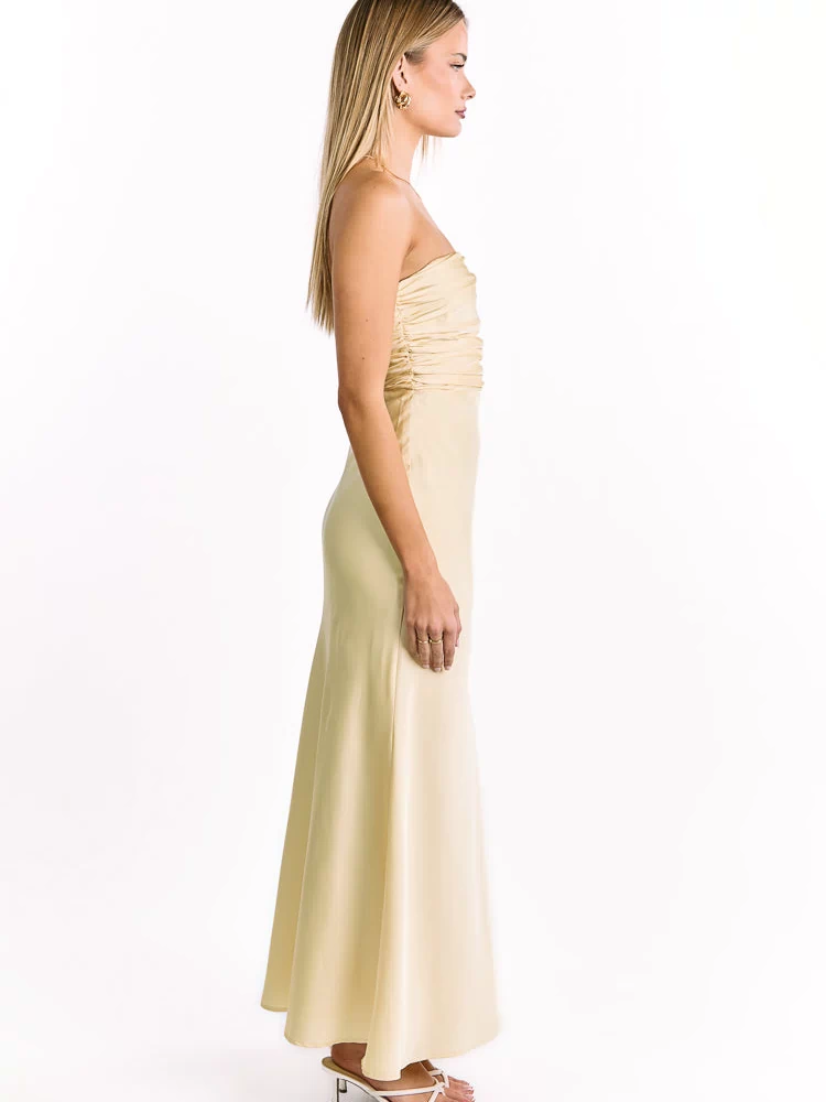 Side profile of a pale yellow strapless maxi dress showing the ruched bust and long flowing skirt