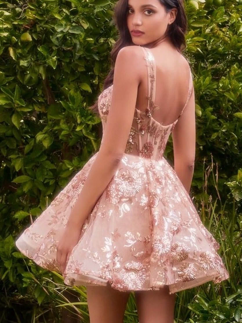 Woman in a Short Sequin-Print Babydoll Hoco Dress A1347 stands outdoors with green foliage behind her, looking over her shoulder.
