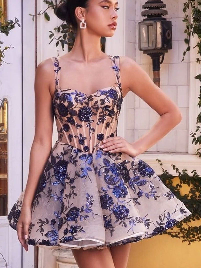 Outdoors, a woman wears the Short Sequin-Print Babydoll Hoco Dress A1347—a sleeveless, fitted dress with a flared skirt and blue and black floral embroidery over a sheer nude base.