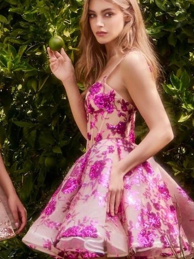 A woman in the Short Sequin-Print Babydoll Hoco Dress A1347 stands outdoors, holding a green fruit amid lush greenery.