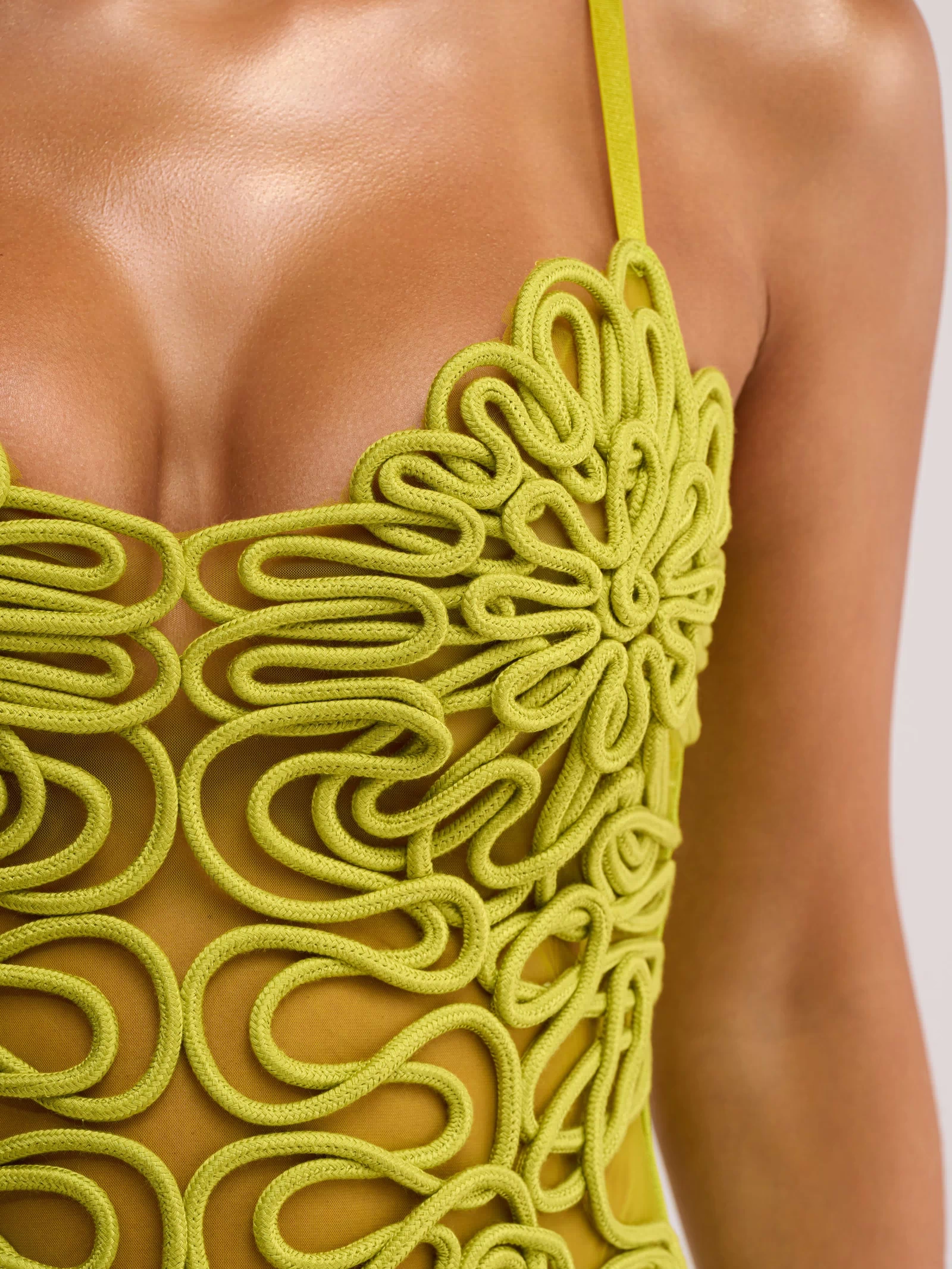 Close-up of a woman wearing the ANYTHING BUT BASIC MINI DRESS IN GREEN, featuring swirling corded patterns, floral motifs, and sheer sections on the chest and torso—ideal as a chic cocktail party dress.