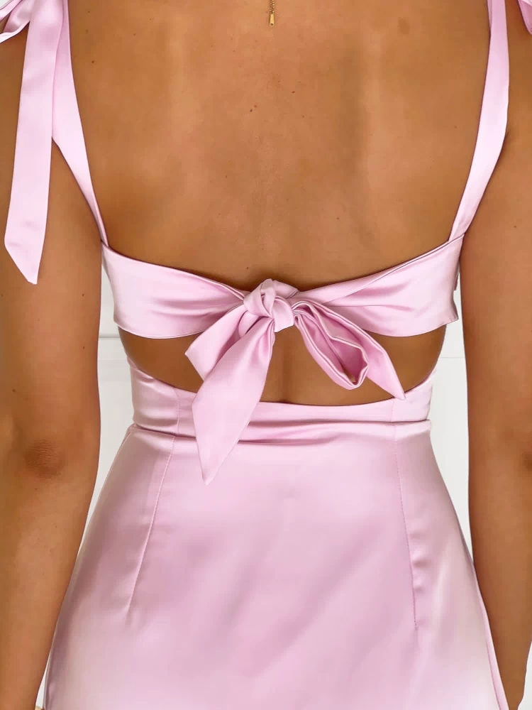 Rear view of a pink satin mini dress showing the large tie-back detail, waist cutouts, and shoulder ties