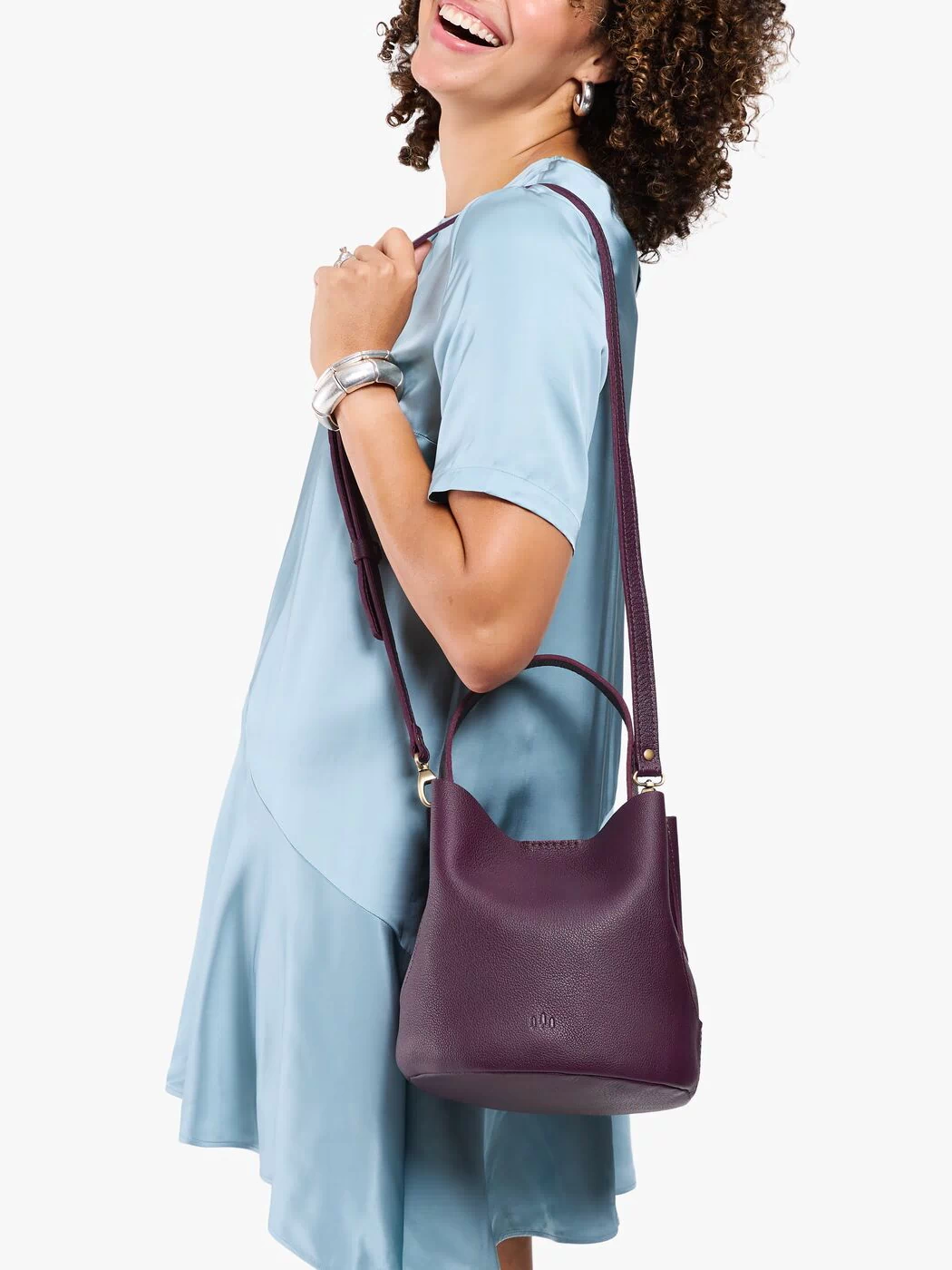 Plum*Large | Model carrying symmetrical bucket bag with handle, latch closure, and removable crossbody strap