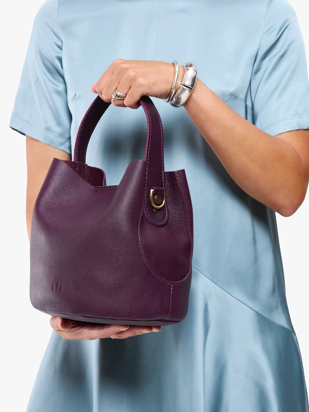 Plum*Large | Model carrying symmetrical bucket bag with handle, latch closure, and removable crossbody strap