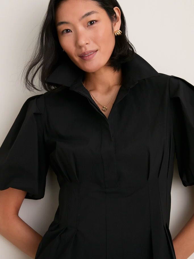 Woman wearing the Black Mini Delaney Dress with a spread collar and puff sleeves, accessorized with gold jewelry, embodying a classic, effortless, and high-end look.