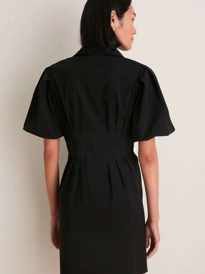 Person wearing the Black Mini Delaney Dress, featuring a classic spread collar and effortless puff sleeves, embodies a high-end, fun style that transitions seamlessly from work to play.