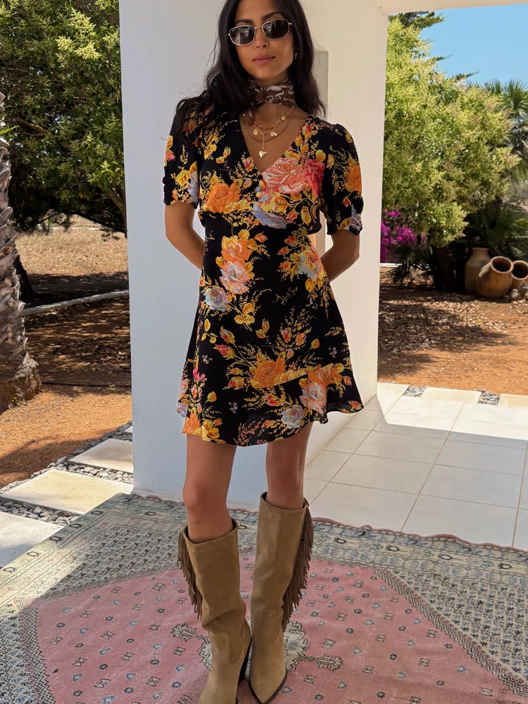 Black Sofia Mini Tea Dress with an intricate floral print and frill hem, styled with tan fringe boots for a vacation look.