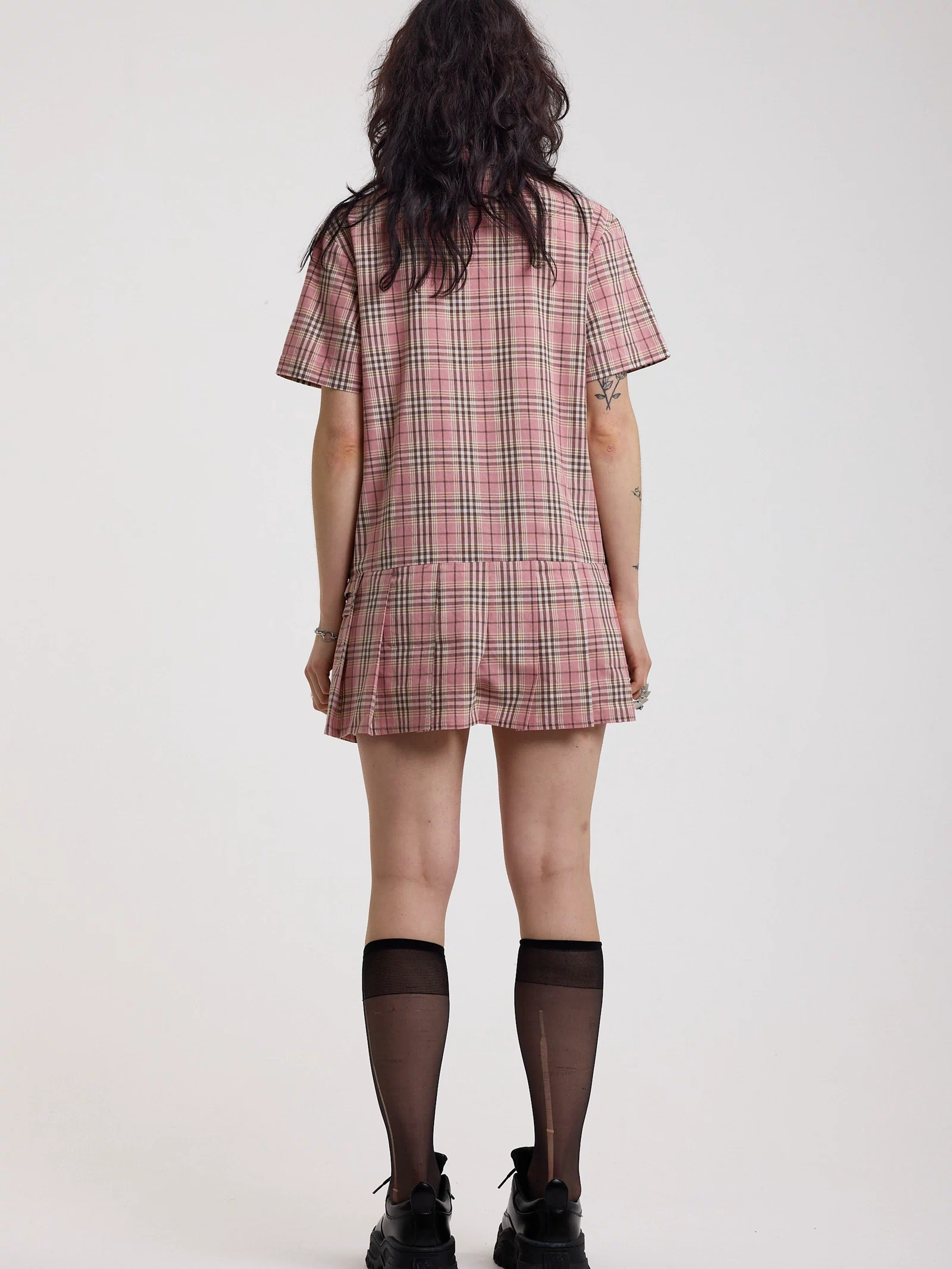Back of pink tartan check mini dress with pleated mini skirt buttons, collar and silver buckle detail, worn by model