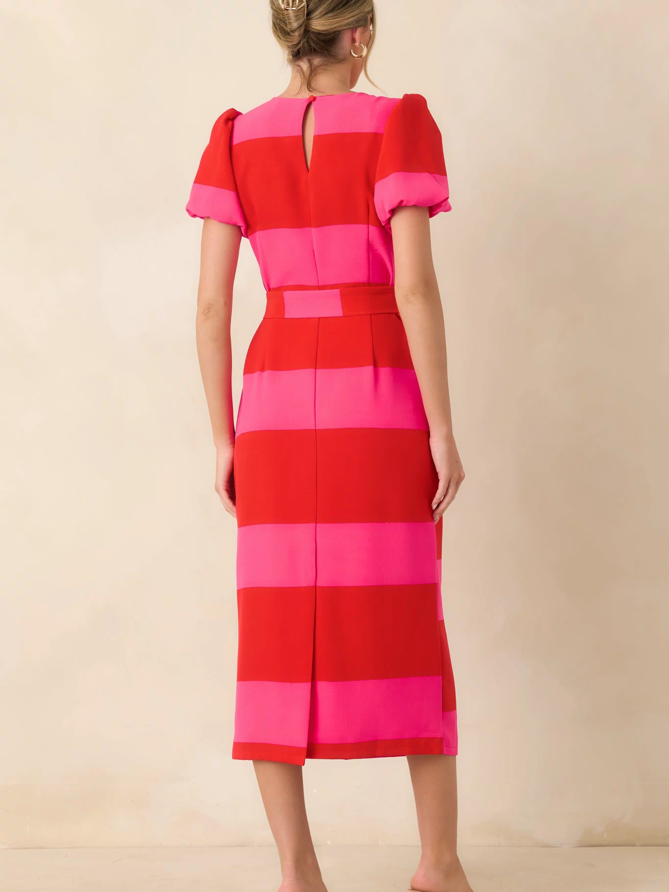 Back view of the red and pink striped midi dress featuring a keyhole button closure and back slit.