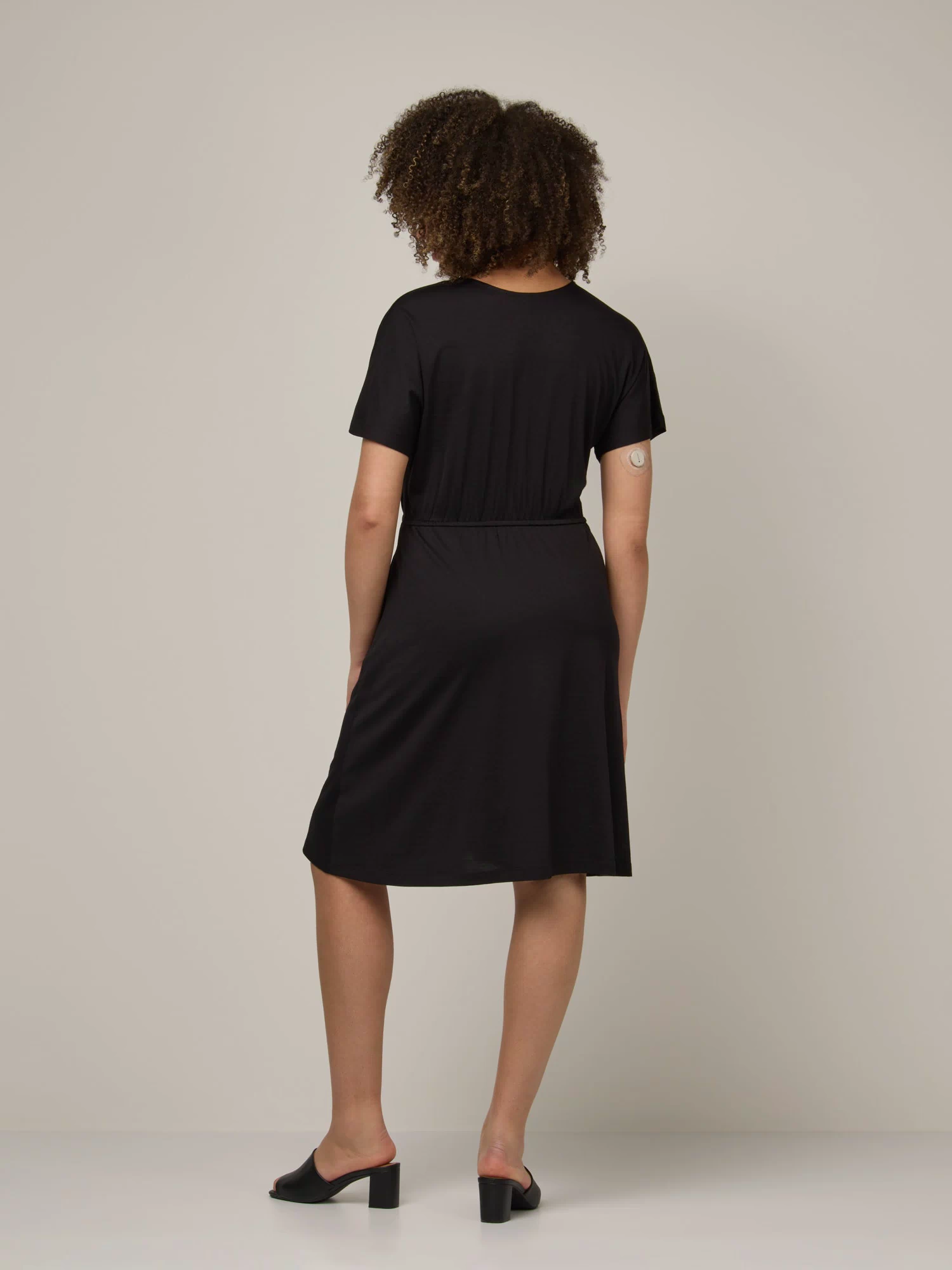 Model wearing Brooklyn Reversible Dress in Black. Brooklyn Reversible Dress is a merino wool short sleeve, reversible, knee length fit & flare dress with pockets available in sizes XS-3X Regular, XS-XL Long.