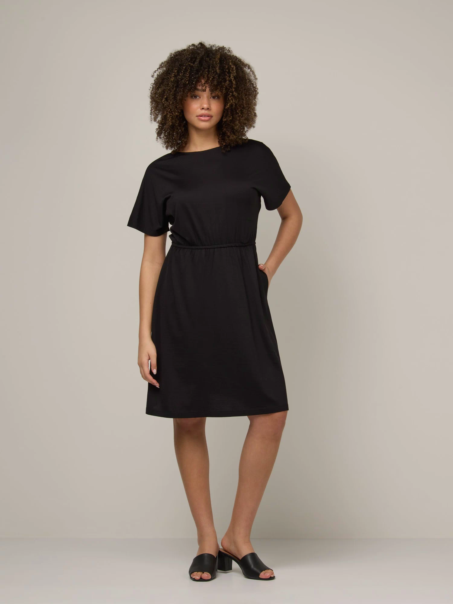 Model wearing Brooklyn Reversible Dress in Black. Brooklyn Reversible Dress is a merino wool short sleeve, reversible, knee length fit & flare dress with pockets available in sizes XS-3X Regular, XS-XL Long.