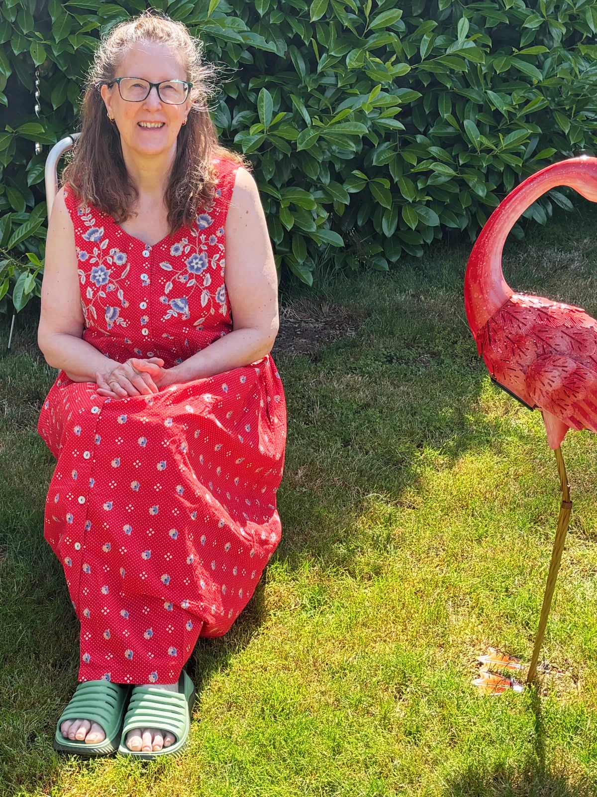 Barbara in a red dress sitting on grass next to a pink flamingo statue.