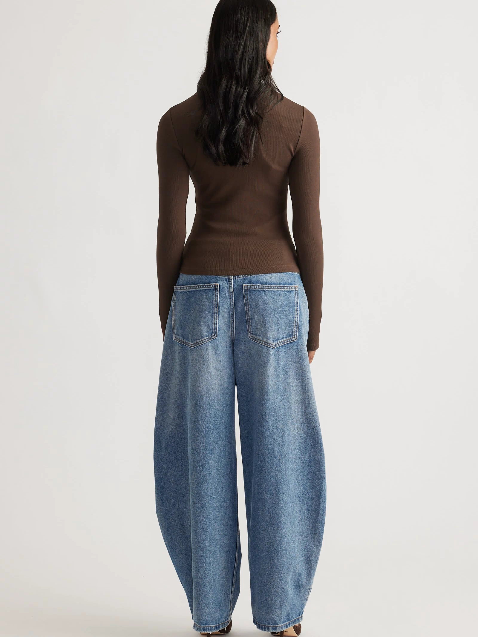 Back view of a slim-fit brown long sleeve top paired with relaxed wide-leg blue denim jeans and heels.