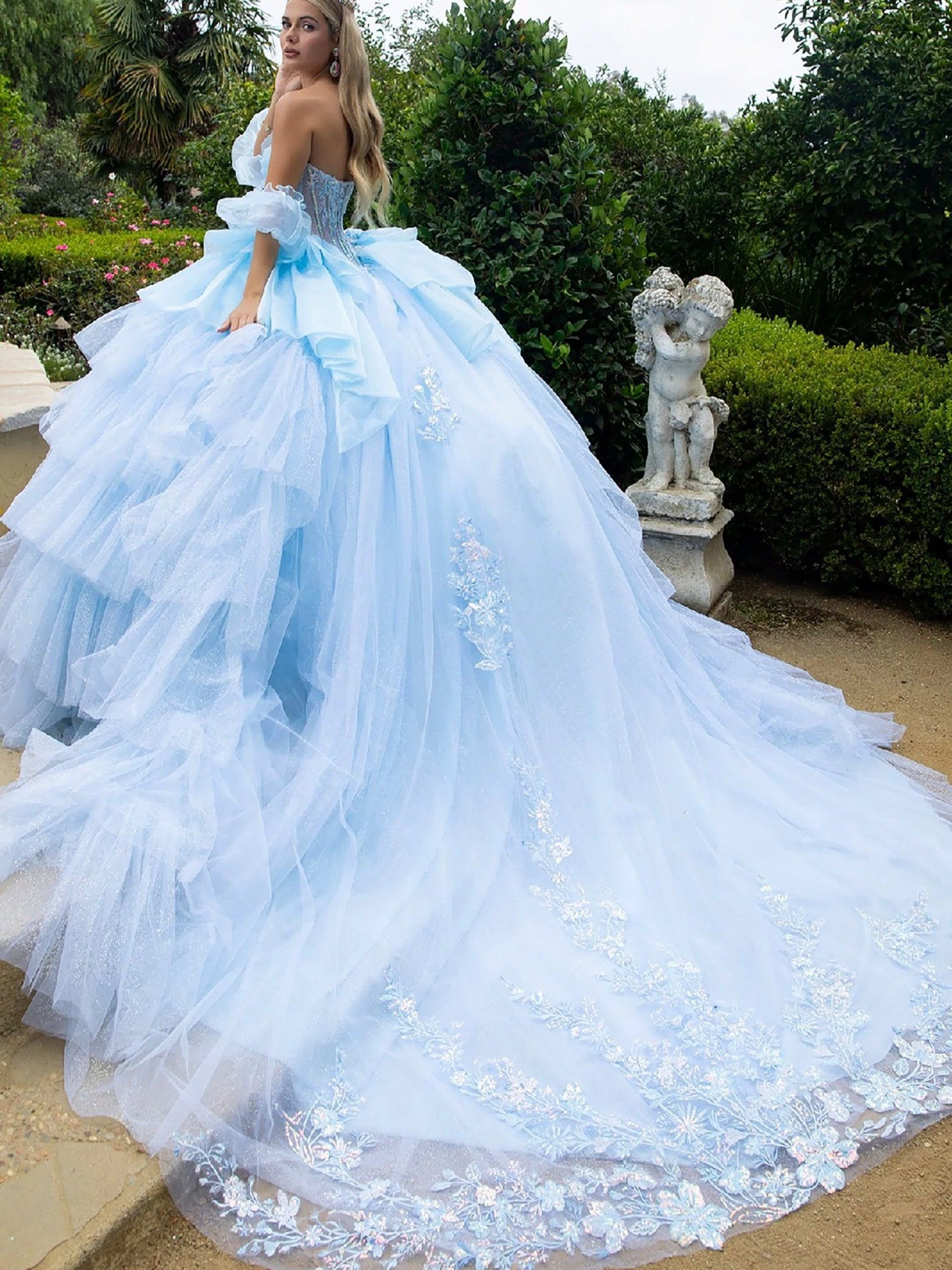 Back view of a woman wearing cinderella blue quinceañera dress with detachable sleeves, layered ruffles, and long train
