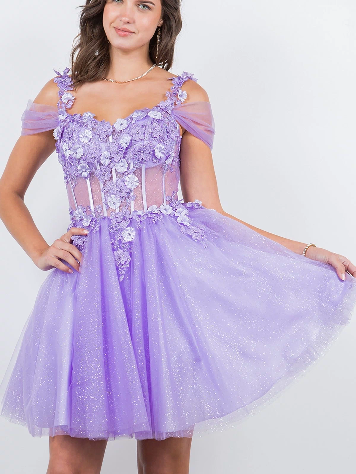 A young woman poses against a plain white background wearing the Embellished Short Glitter-Tulle Homecoming Dress, a sparkly lilac off-shoulder fit-and-flare style with floral appliqué details.