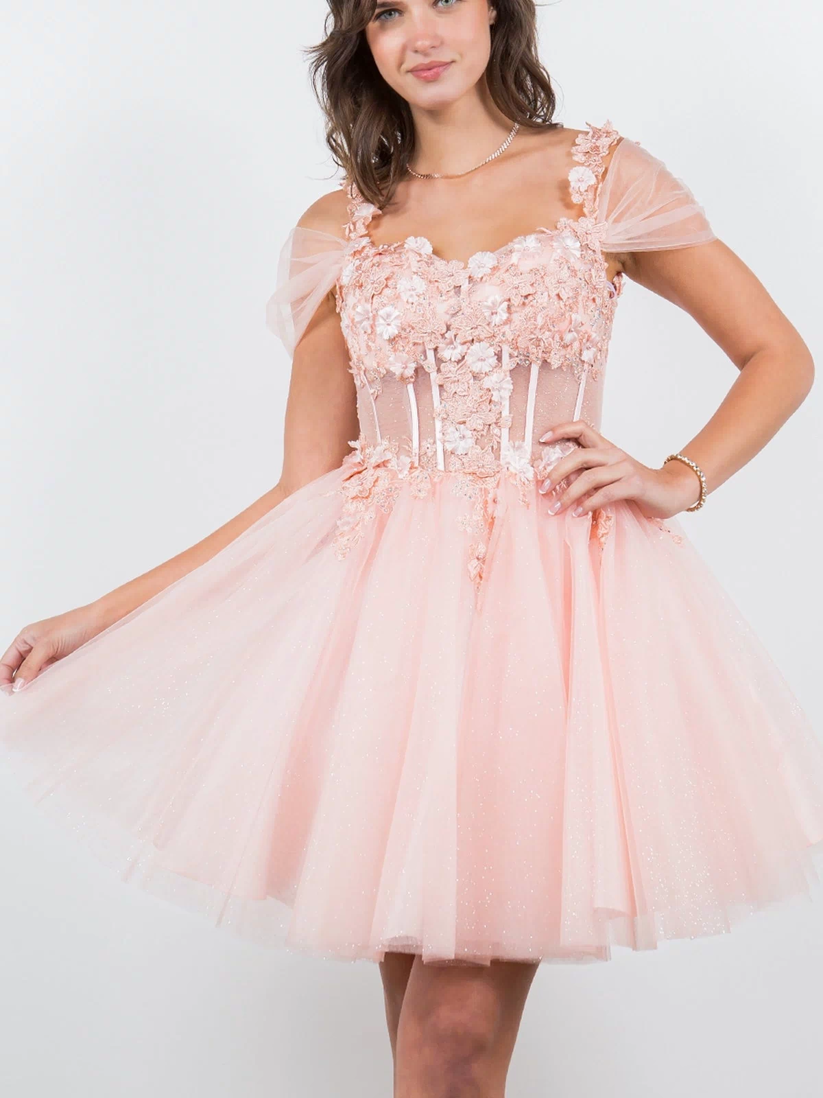 A woman wears the Embellished Short Glitter-Tulle Homecoming Dress, featuring light pink floral appliqué and sheer cap sleeves, standing against a plain white background.