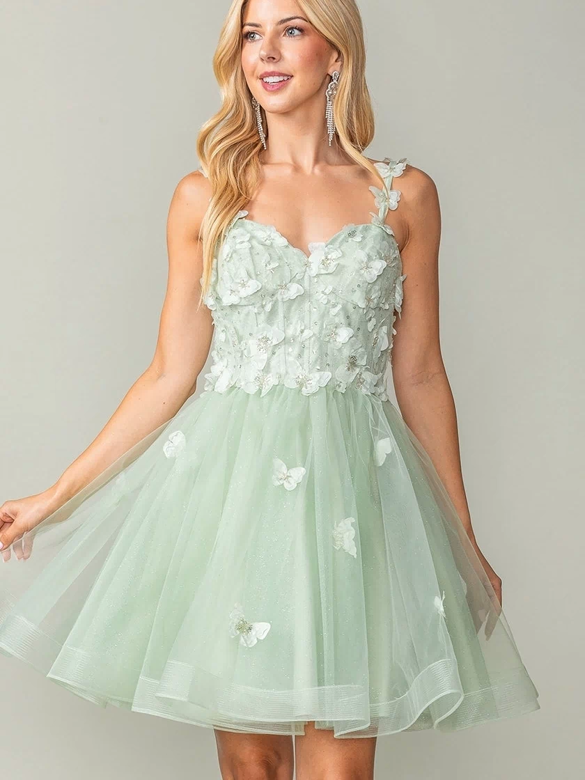 A woman wears the Lace-Up Short Butterfly Homecoming Dress 3369, a light green knee-length semi-formal dress featuring floral appliqués and 3-D butterflies on a tulle skirt, standing against a plain background.