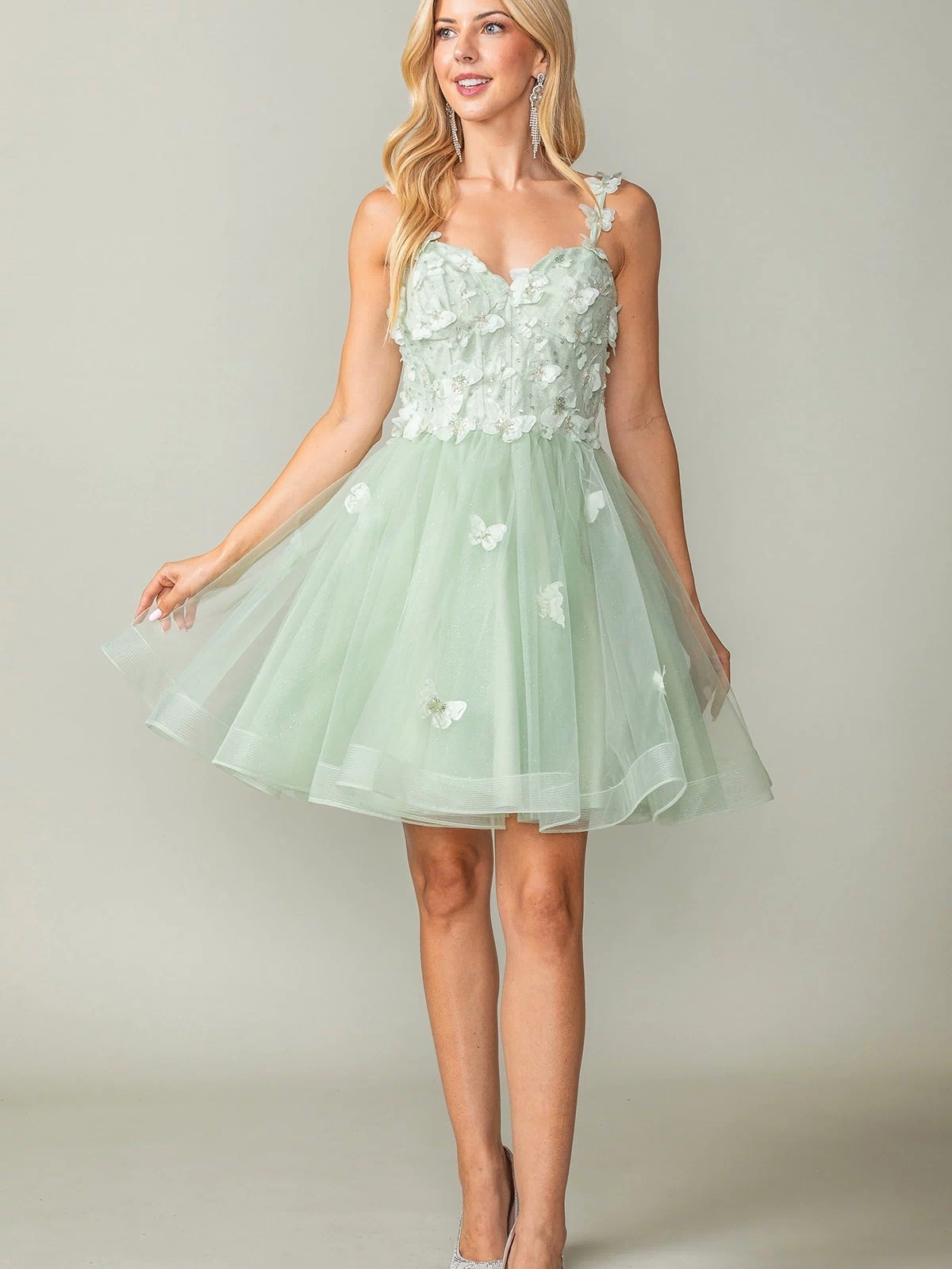 A woman stands against a plain background in the Lace-Up Short Butterfly Homecoming Dress 3369—mint green, knee-length tulle with 3D butterflies and floral appliqués—paired with silver heels.