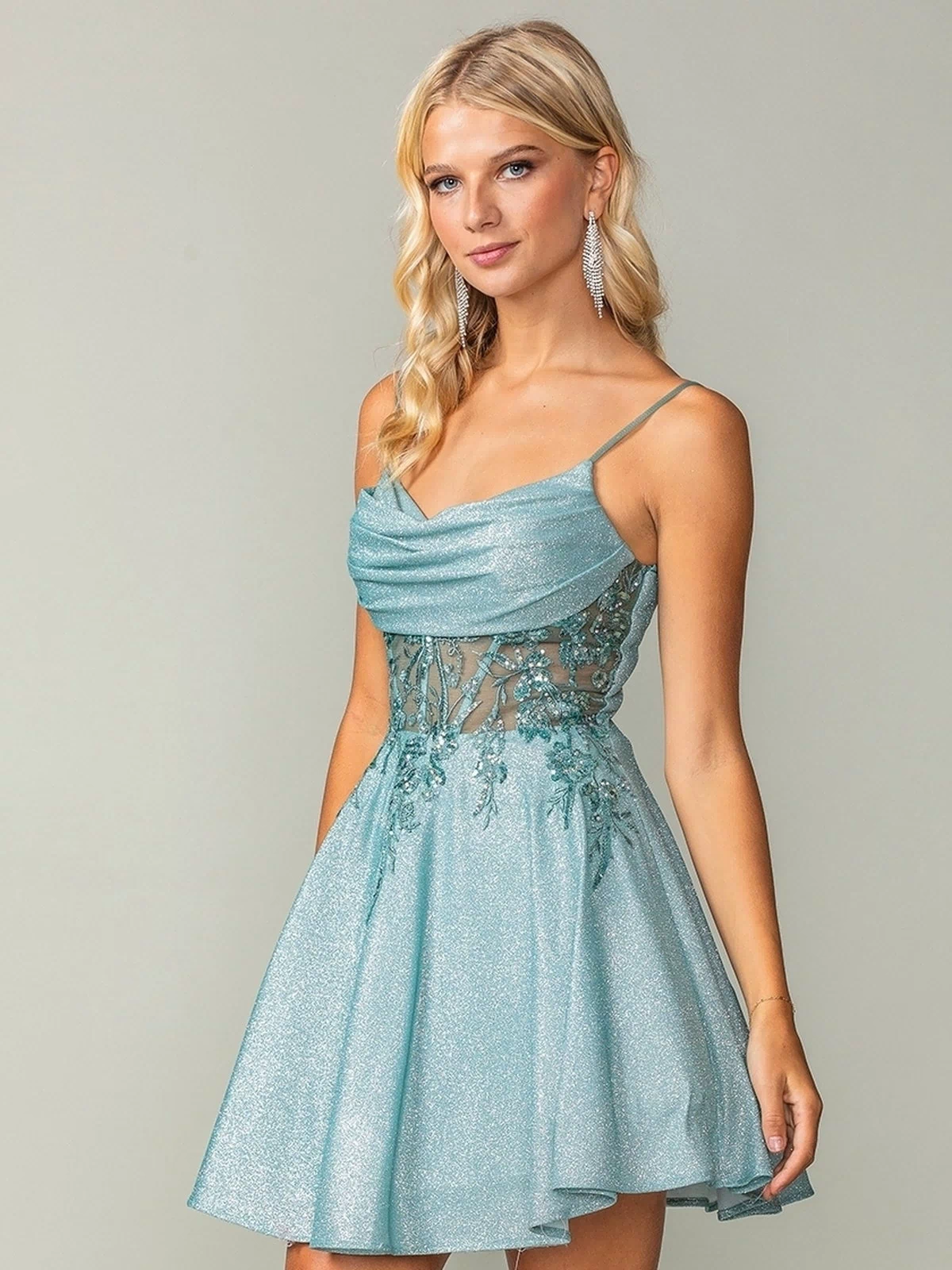 A woman models the Cowl-Neck Short Glitter Homecoming Dress 3386, a light blue, sleeveless mini dress with spaghetti straps, lace bodice, cowl neckline, and flared skirt against a plain background.