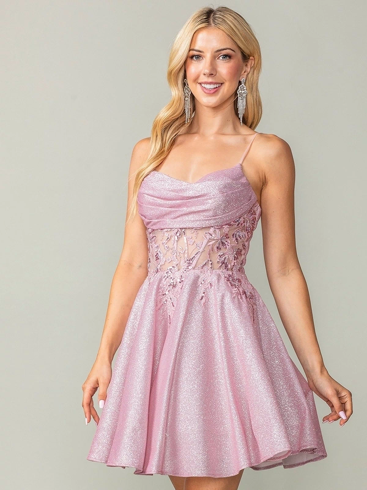 A woman wears the Cowl-Neck Short Glitter Homecoming Dress 3386, featuring floral lace bodice details, as she stands smiling against a plain background.