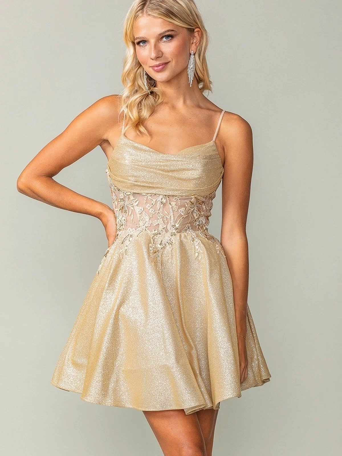 A woman poses in the Cowl-Neck Short Glitter Homecoming Dress 3386, a sleeveless gold party dress featuring sheer embroidered waist detailing, against a plain background.
