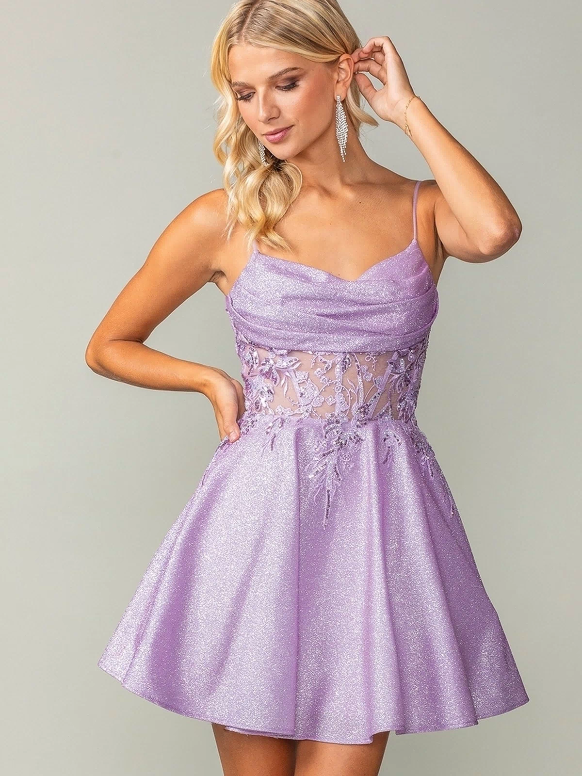 Woman wearing the Cowl-Neck Short Glitter Homecoming Dress 3386 in lavender, featuring a sleeveless sheer lace bodice and flared skirt, poses with one hand touching her hair.