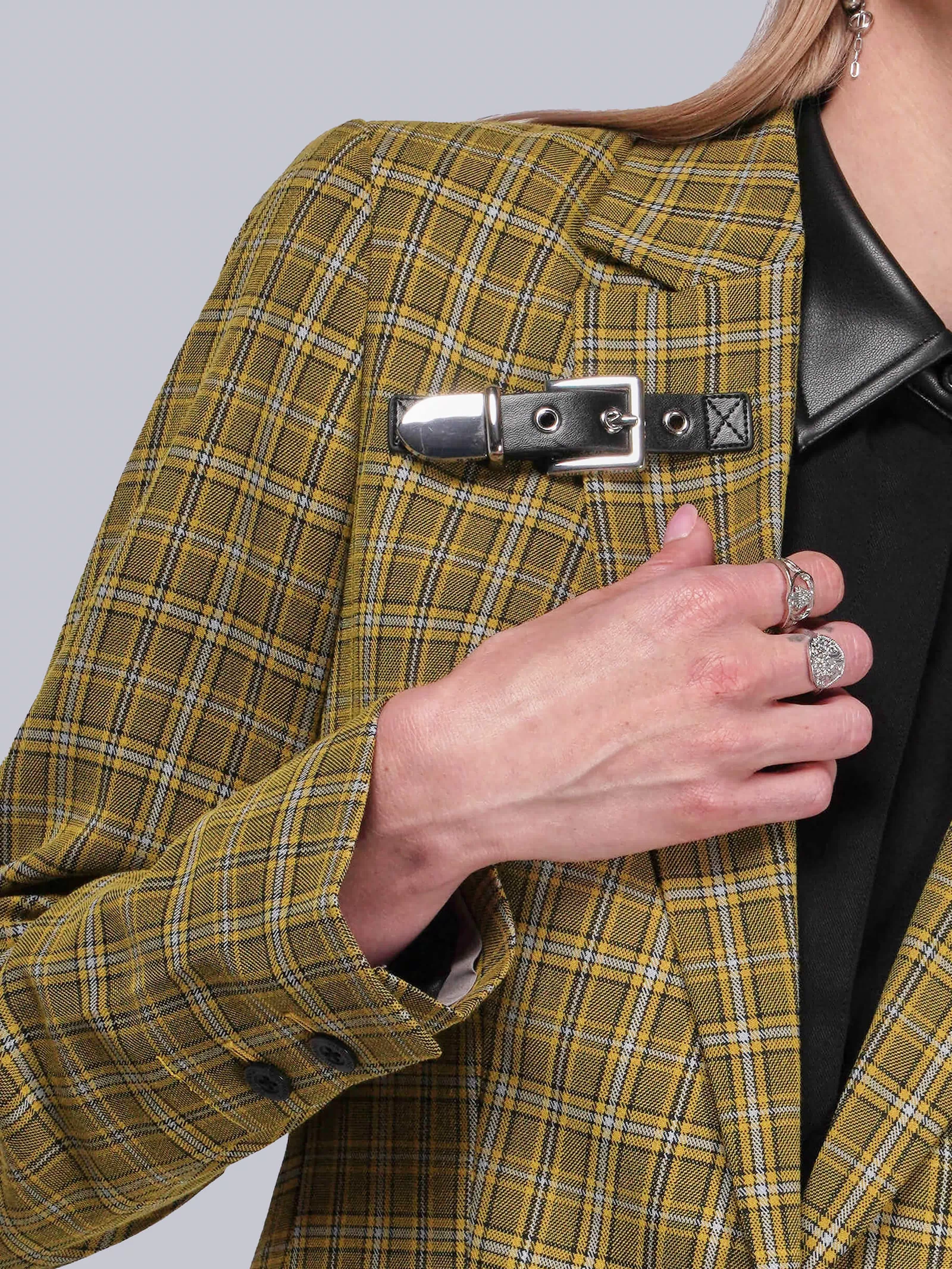 S=Person wearing a yellow plaid blazer with a black leather buckle detail on a plain background