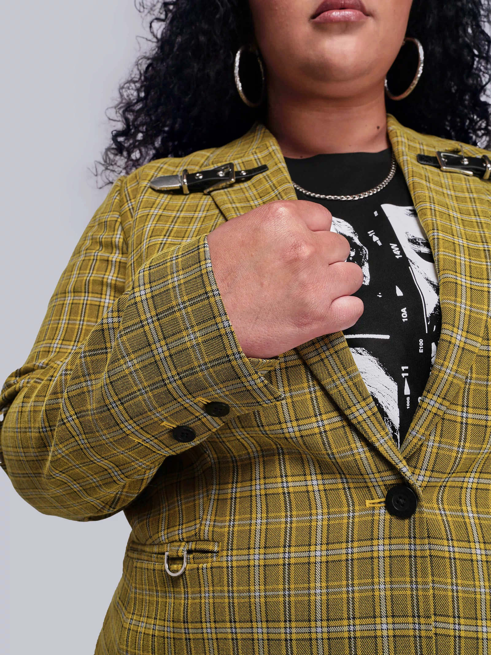 1X=Close up view of person wearing a yellow plaid jacket with black buttons on a plain background
