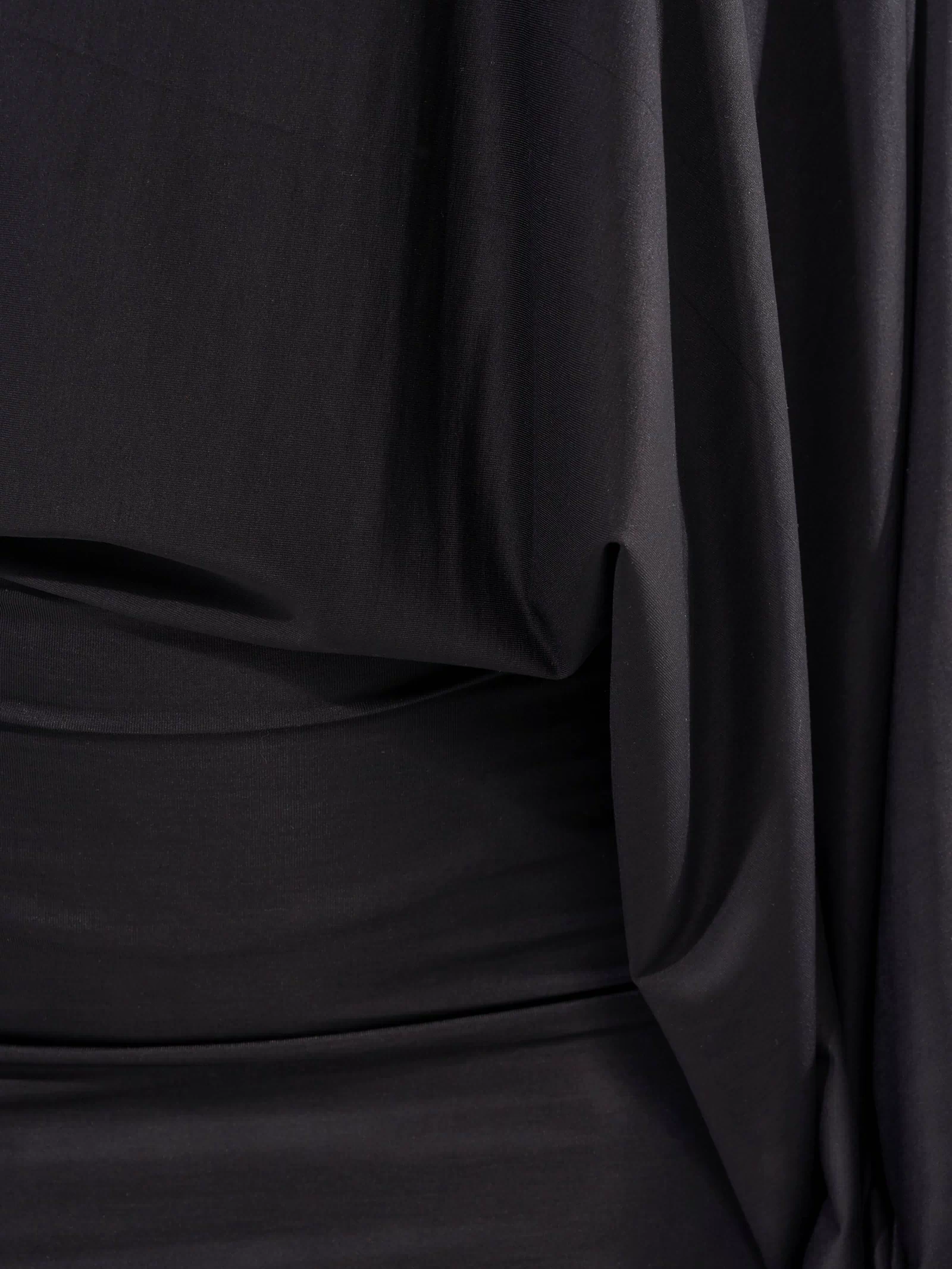 A close-up of the DIANA DRAPED MINI DRESS IN BLACK shows soft folds in the fabric, creating smooth textures and gentle shadows reminiscent of a classic little black dress.