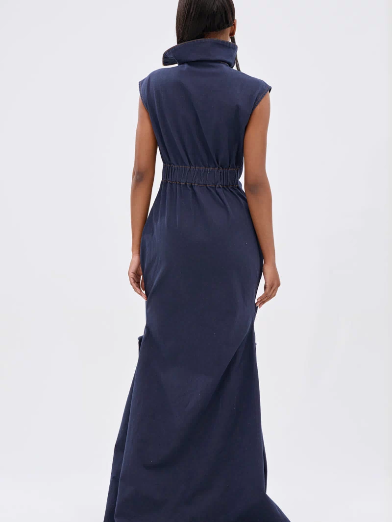 A woman with straight hair stands facing away against a light background, wearing the DONT MESS WITH ME COLLARED DENIM MAXI DRESS featuring a high collar and gathered waist.