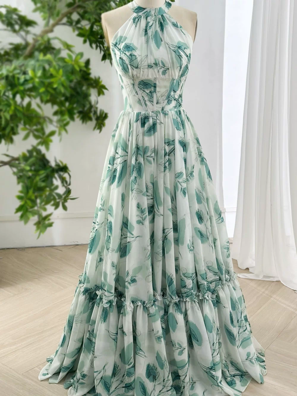 Full length flowy chiffon halter gown in botanical green print with gathered waist and ruffled skirt for evening formal events