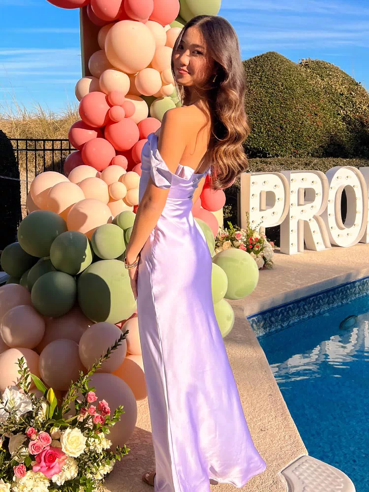 Side profile of the lilac off-shoulder maxi dress, highlighting the draped sleeves and smooth satin fabric