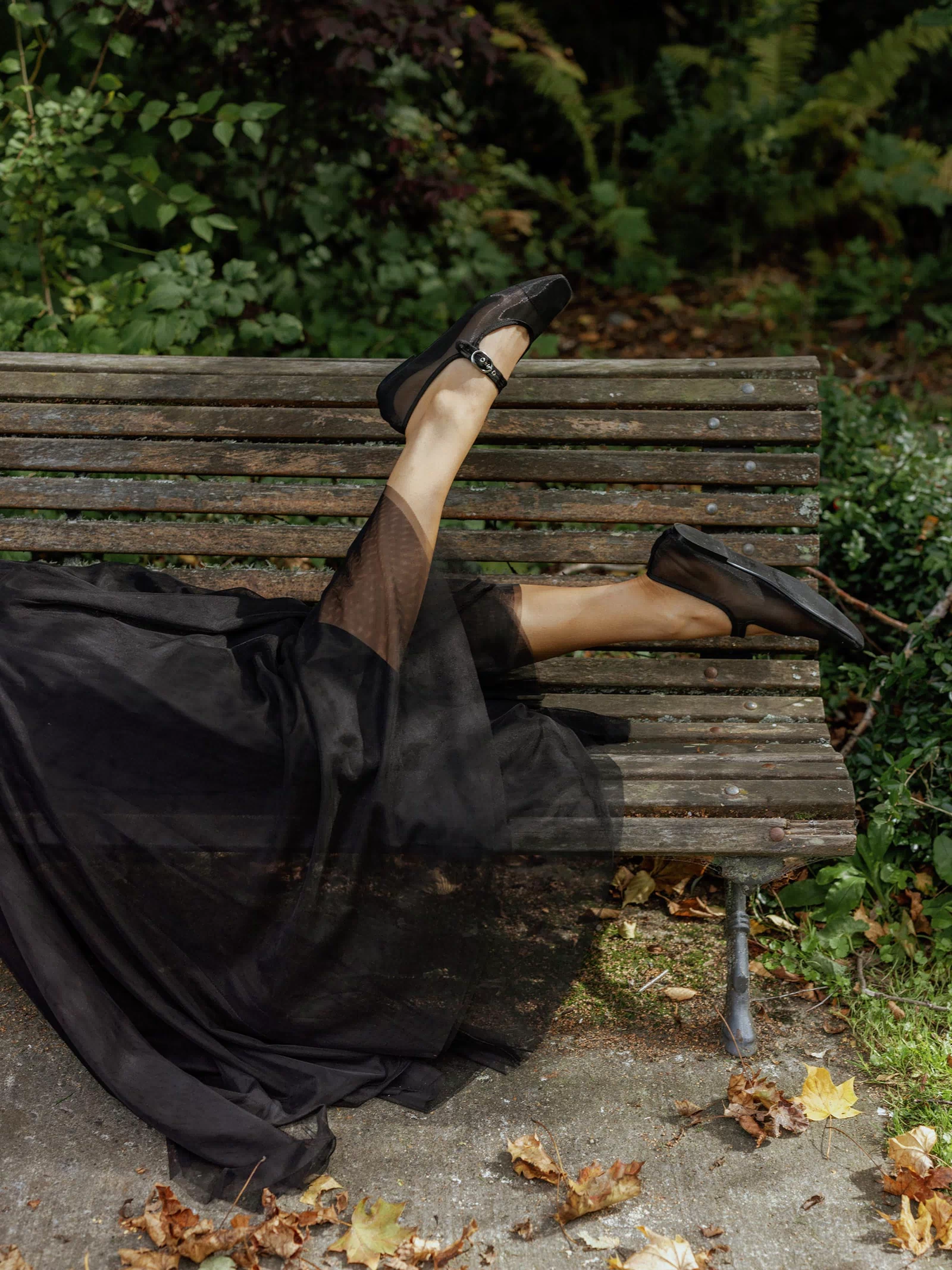 Person in Max Emilie Tulle Skirt lounges on a park bench, legs raised among autumn leaves.