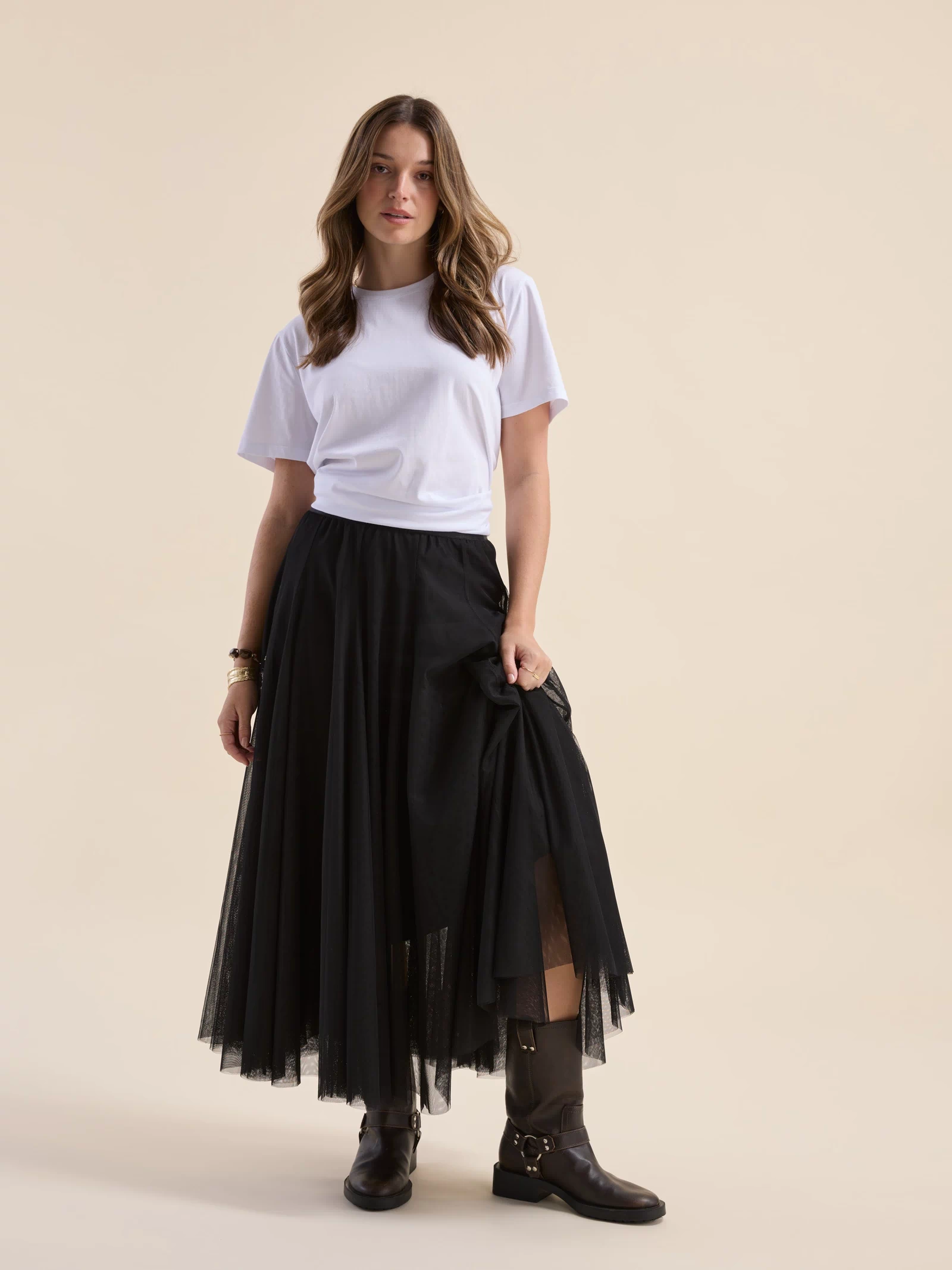 Woman in a white tee, Max Emilie Tulle Skirt, and boots stands against a beige background.