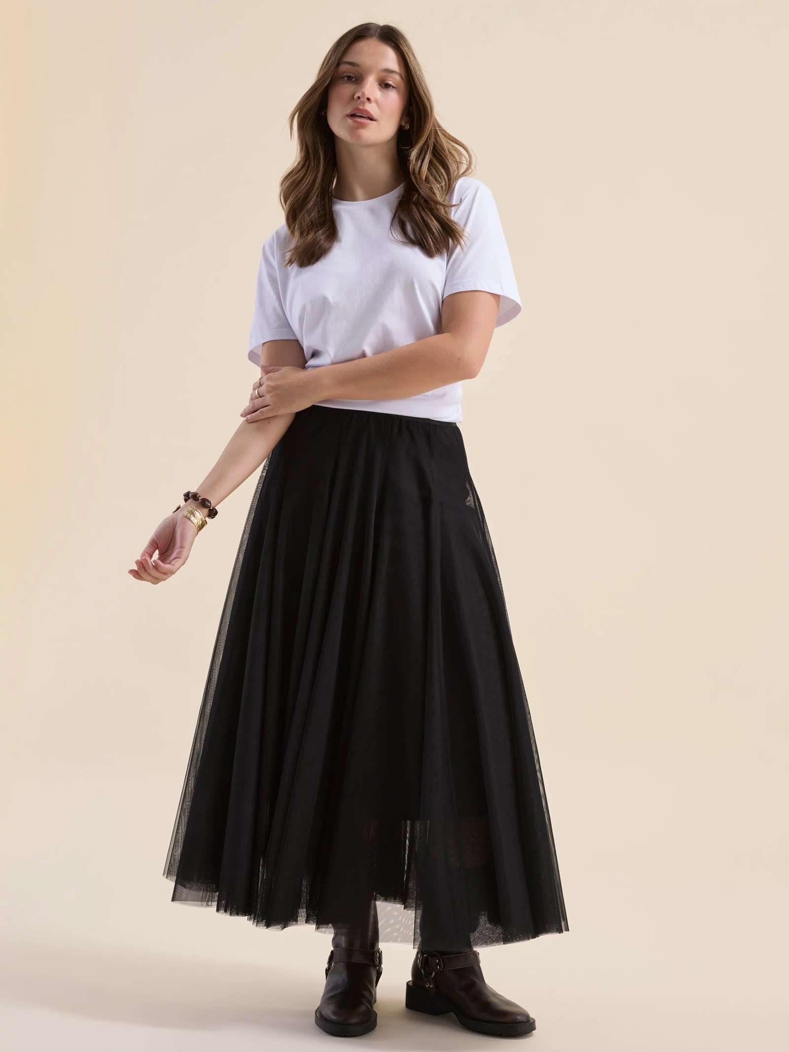 Woman in Emilie Tulle Skirt by Max, white tee, and boots poses against a beige background.