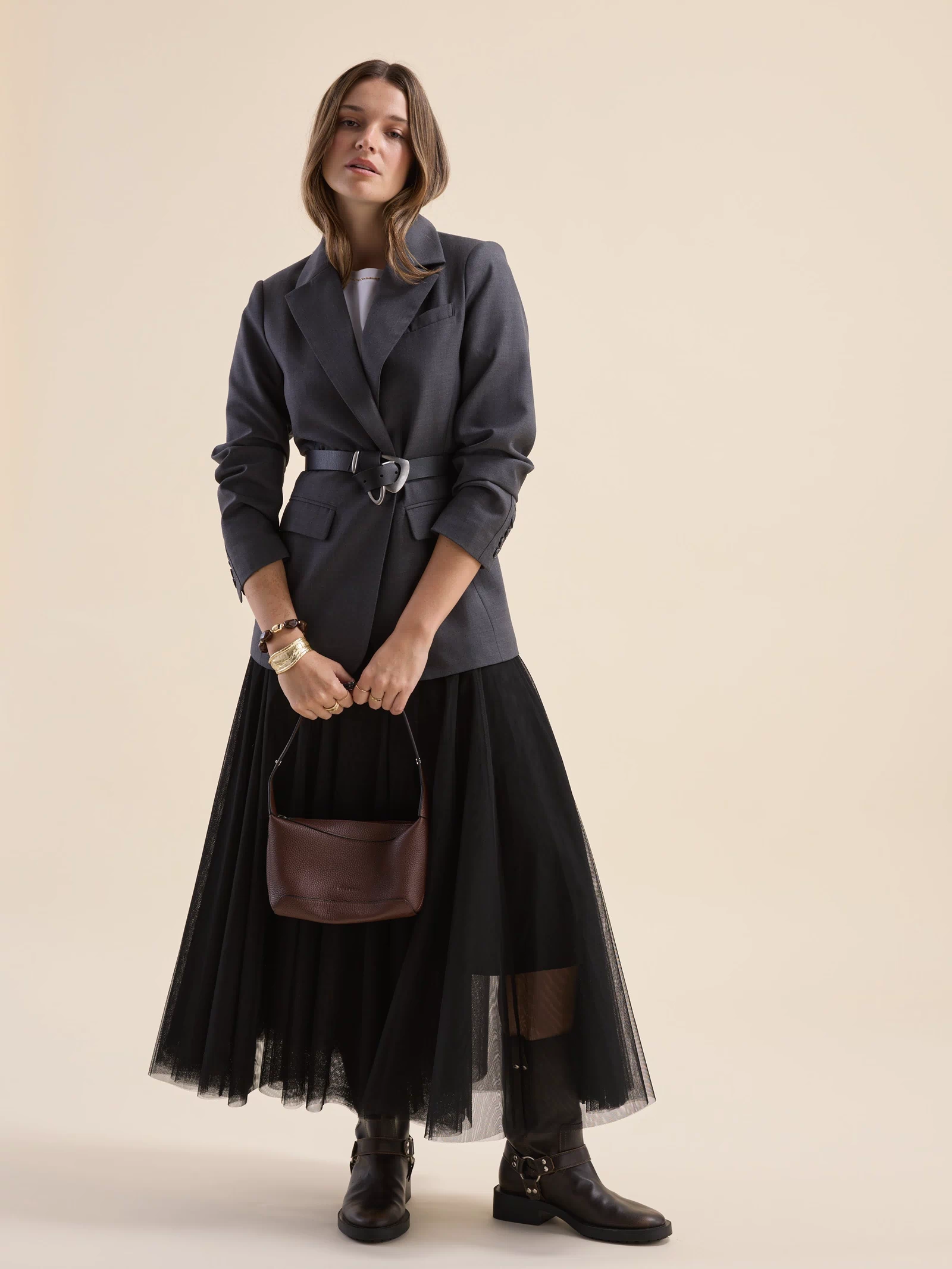 Woman in blazer, Emilie Tulle Skirt by Max, boots, brown handbag, beige background.