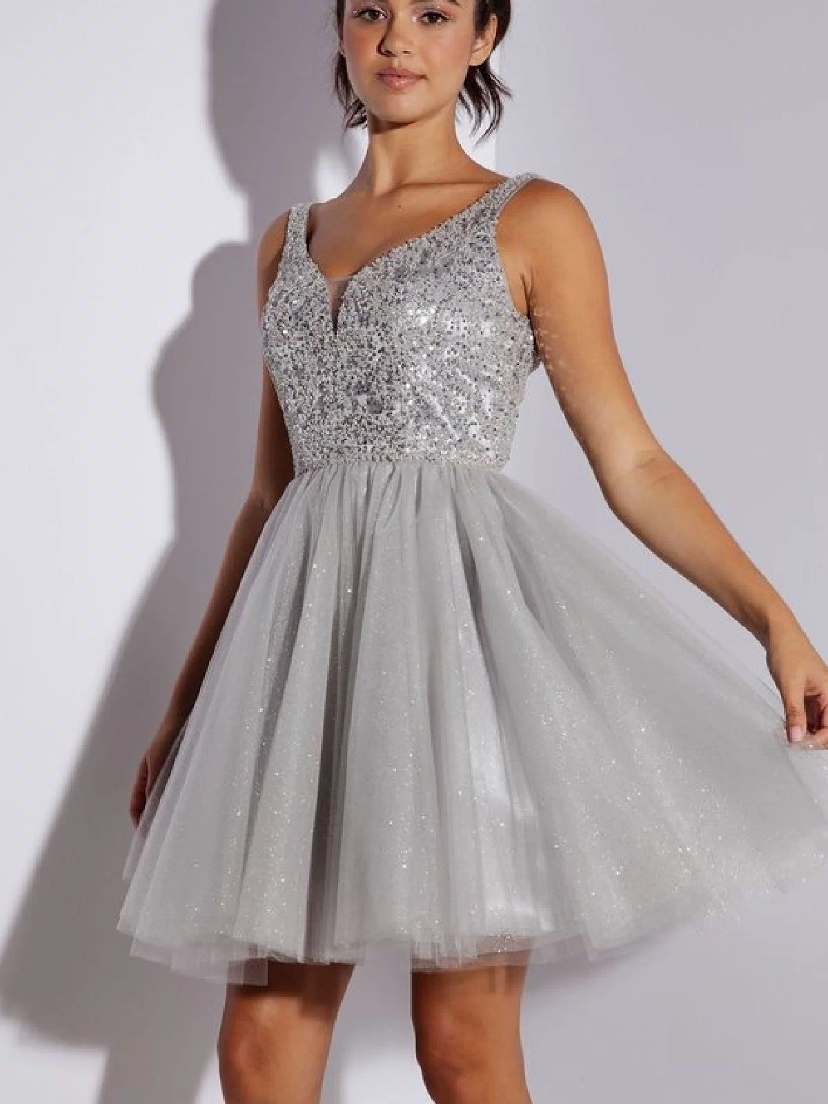 A woman stands against a plain background wearing the Glitter-Bodice Short A-Line Hoco Dress: Eureka 9926, which features a sequin bodice and flared tulle skirt.