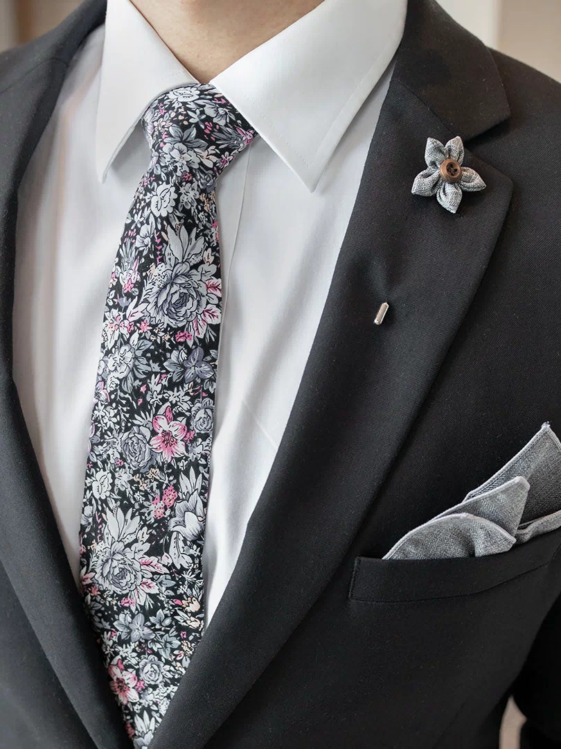 Floral Black cotton tie styled on a model with a black suit jacket, a white shirt, a pocket square and a lapel pin