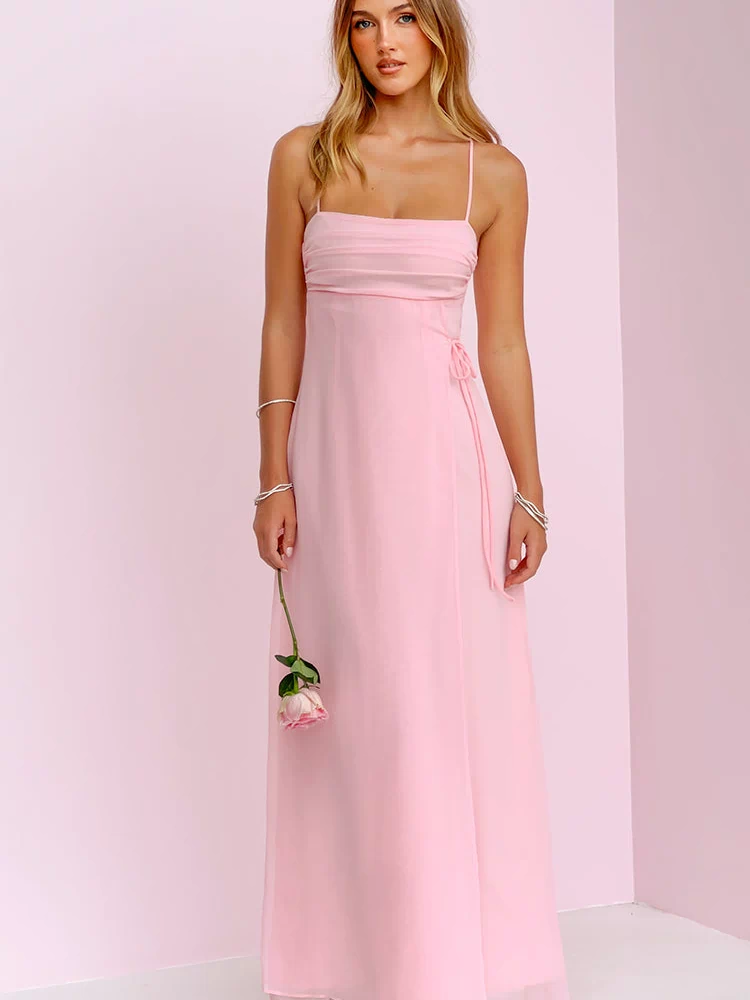 Front view of a pink sleeveless maxi dress with a ruched square neckline, thin straps, a side tie, and a flowy sheer overlay skirt