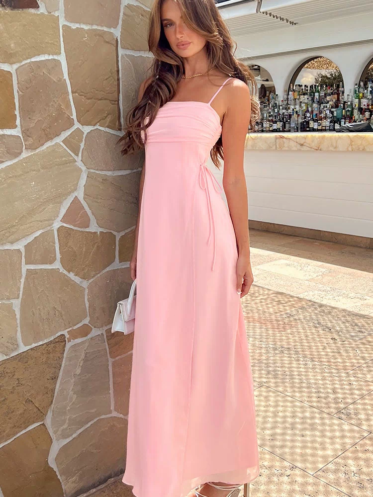 Full length view of a pink maxi dress with a ruched bust, thin spaghetti straps, and side tie details