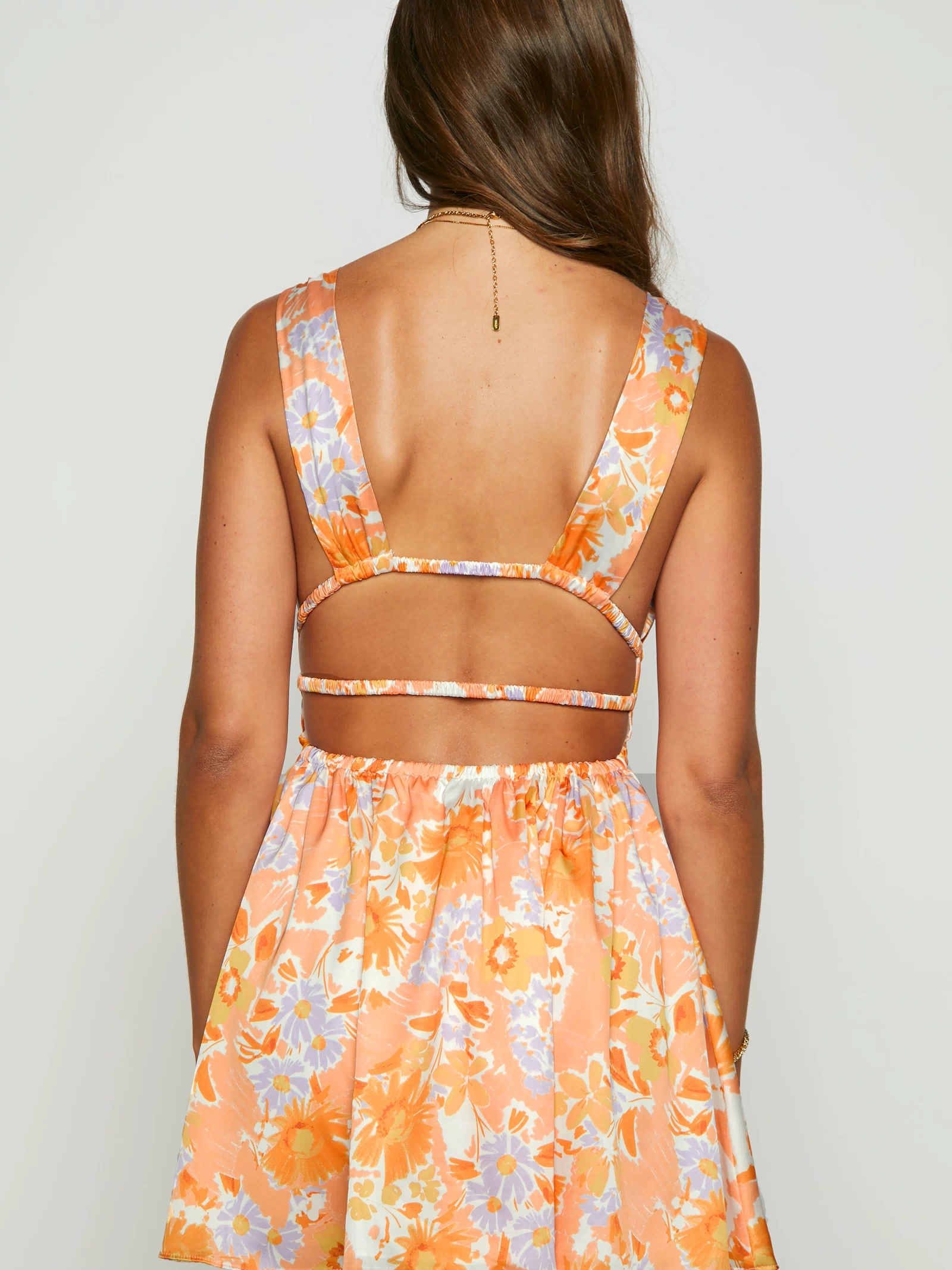 Rear view of an orange floral mini dress showing wide cross-back straps, elasticated back band, and cutouts