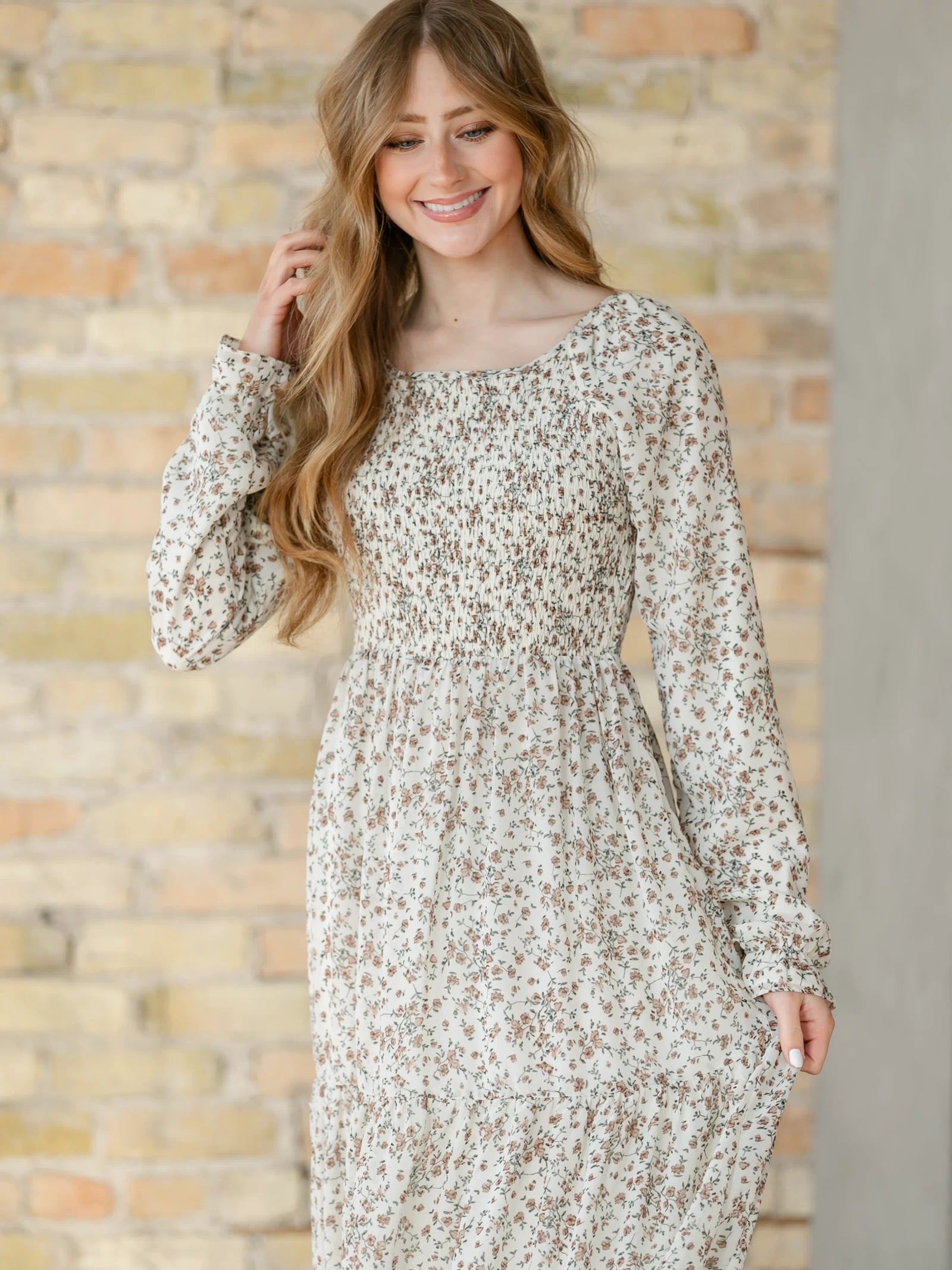 Woman wearing a floral dress against a brick wall.