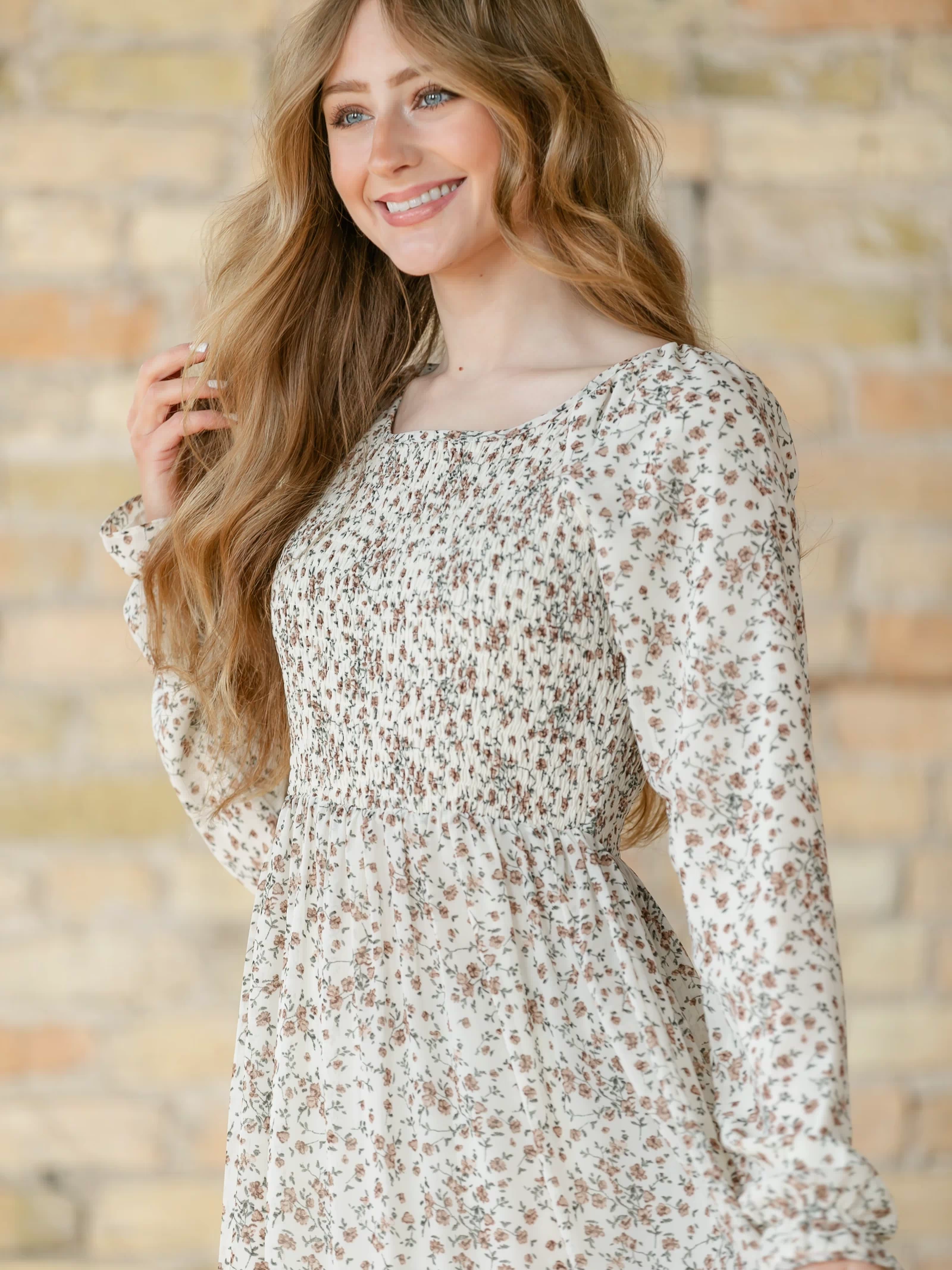 Close-up of a woman wearing a floral dress against a brick wall.