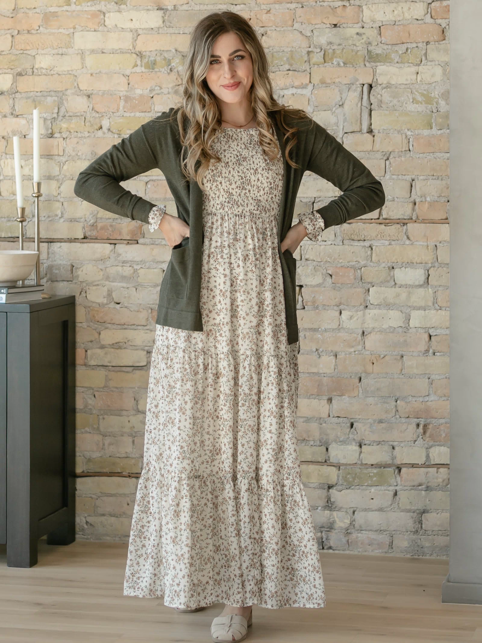 Woman wearing a floral dress and green cardigan against a stone wall.