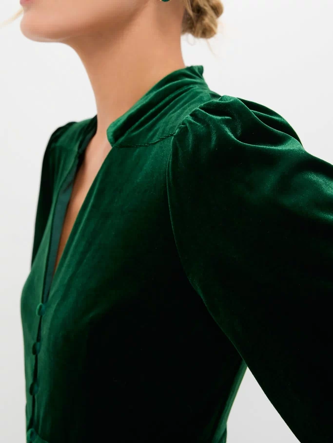 Woman in a classic, high-end Green Velvet Serena Dress with balloon sleeves and button placket, exuding effortless elegance. Paired with matching gemstone earrings for a fun, sophisticated look.