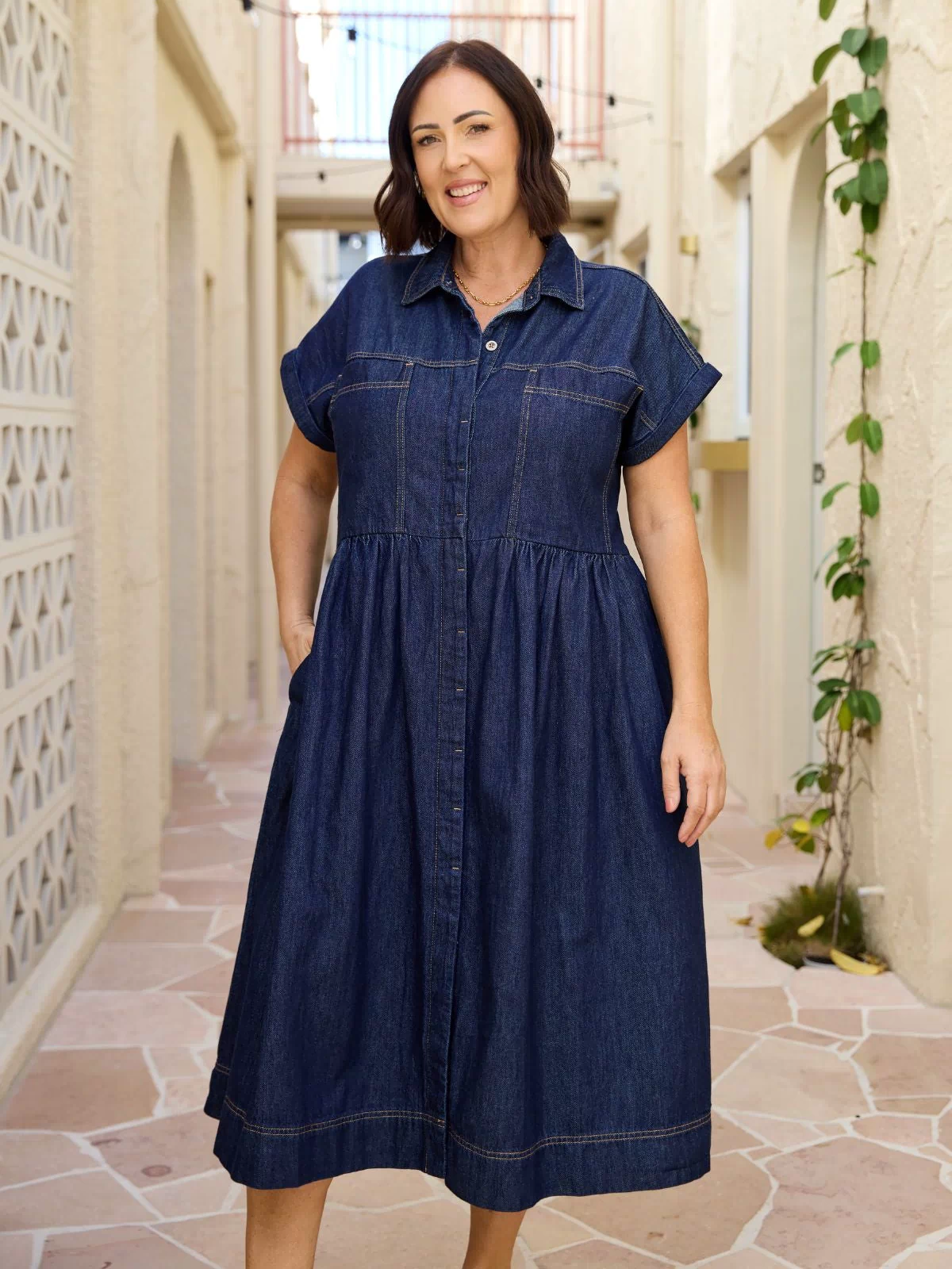 Harper petite denim midi dress shown front on a model, indigo fabric, button placket, short sleeves, defined waist and front pockets.