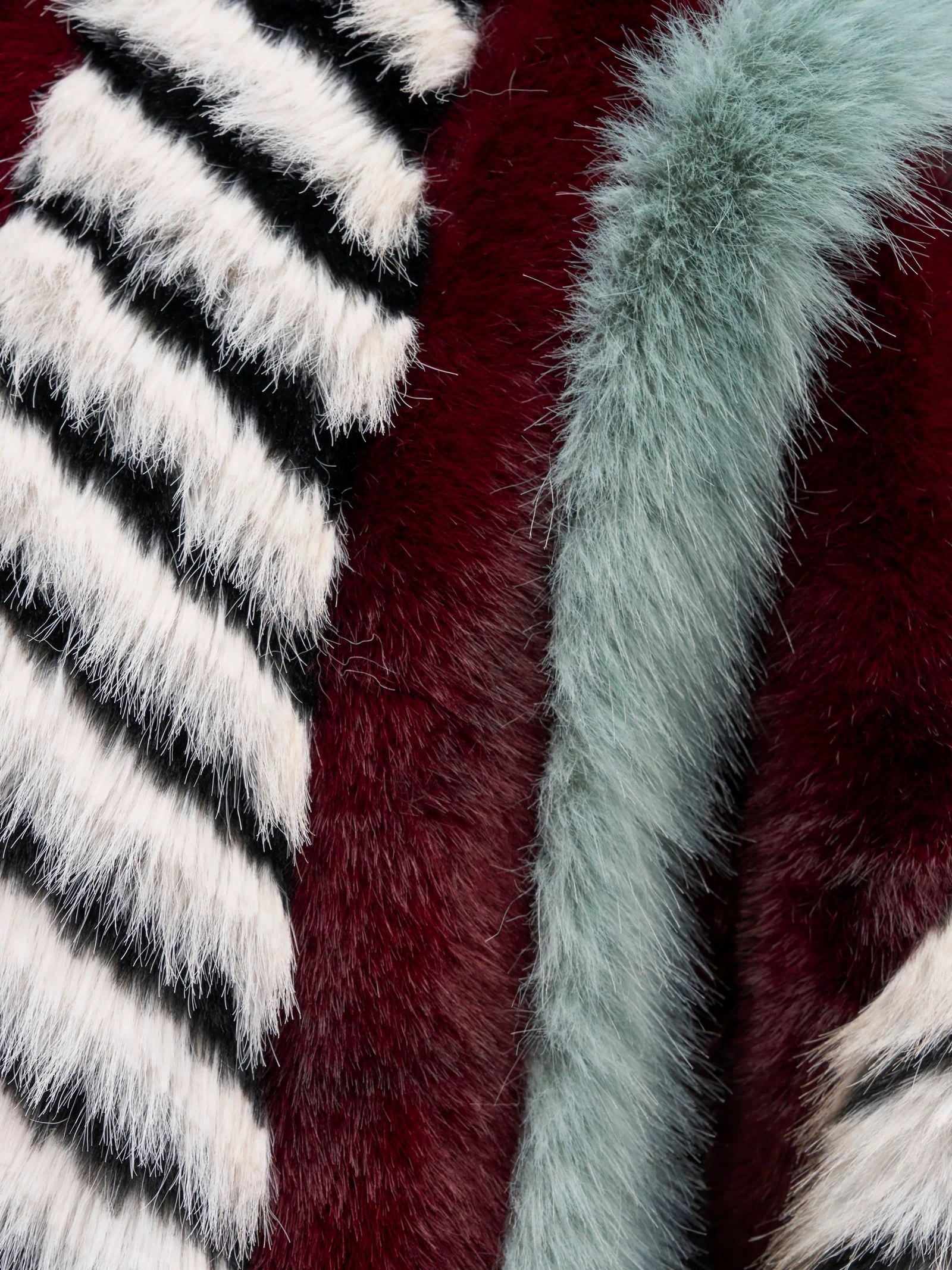 Close-up of the textured fabric on the HAVE IT ALL PANELED FUR COAT, showcasing vertical panels of multicolored faux fur with black and white stripes, rich red, and pale blue-green fuzzy sections.