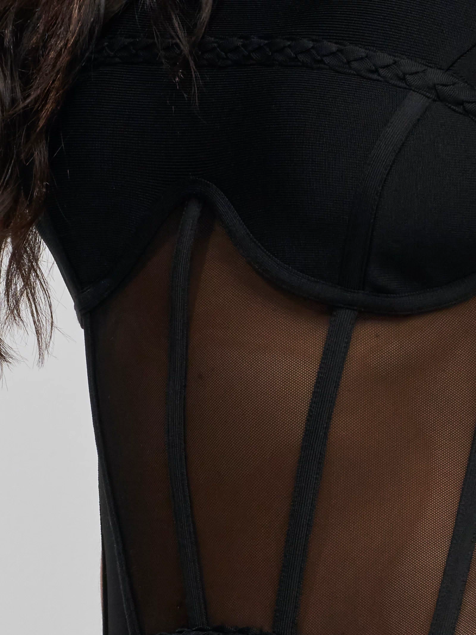 Close-up of a person wearing the ICONIC INSTINCT BANDAGE CORSET MIDI DRESS, featuring sheer mesh panels and braided trim, with part of their back, shoulder, and dark hair partially visible.